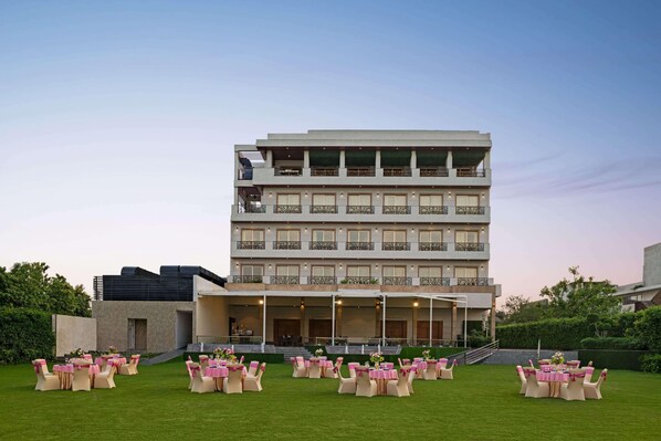 A multi-story hotel with a flat roof, balconies, and a well-maintained lawn with tables and chairs.