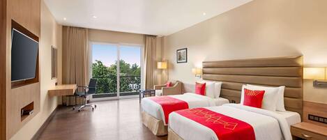 Habitación de hotel con dos camas, televisión, escritorio y balcón con vistas.