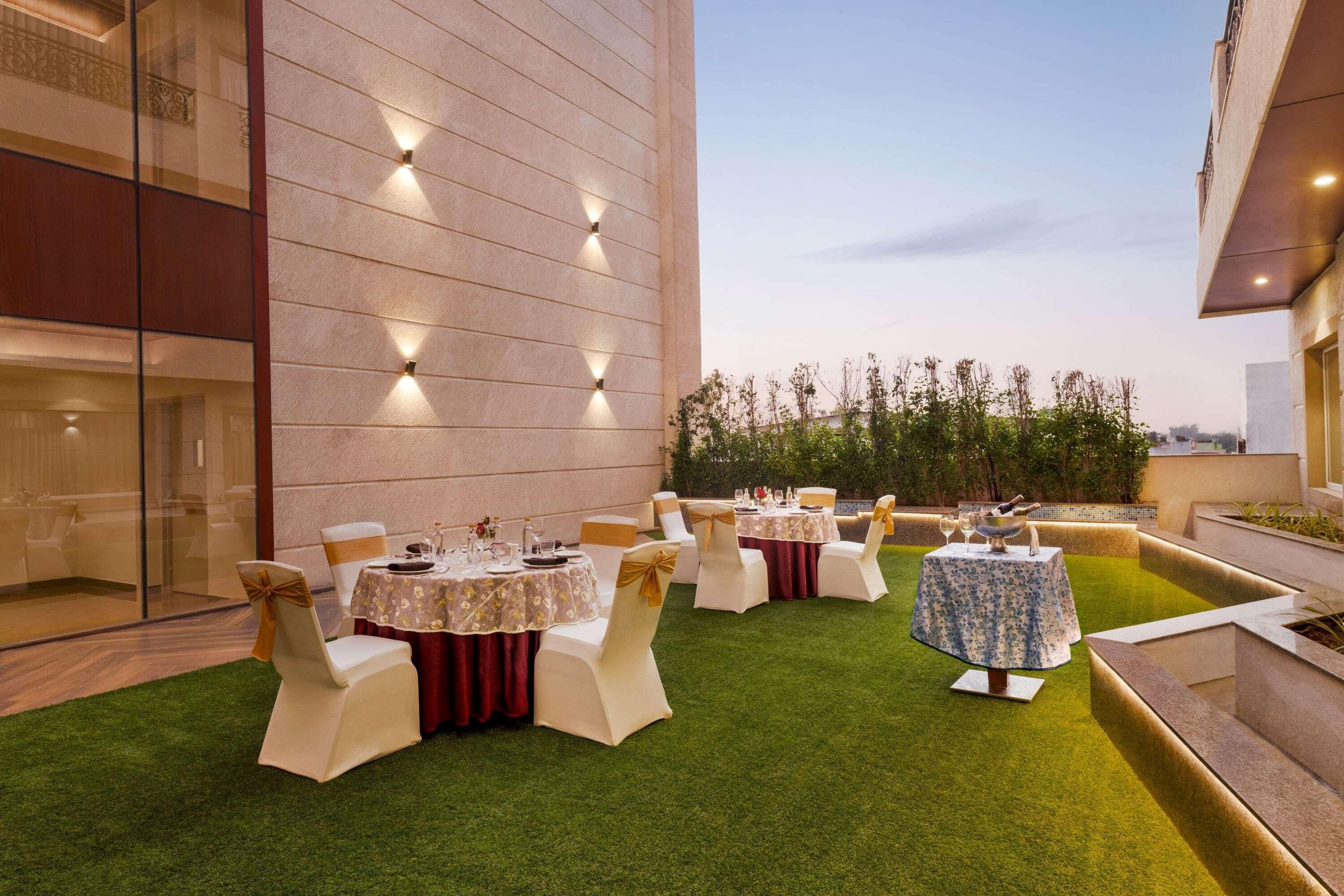 An outdoor dining area with tables and chairs, a building with a modern design, and a clear sky.