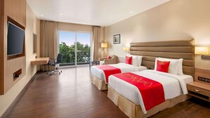 A hotel room with two beds, a TV, a desk, and a balcony with a view. - Ramada By Wyndham Aligarh Gt Road (Aligarh)