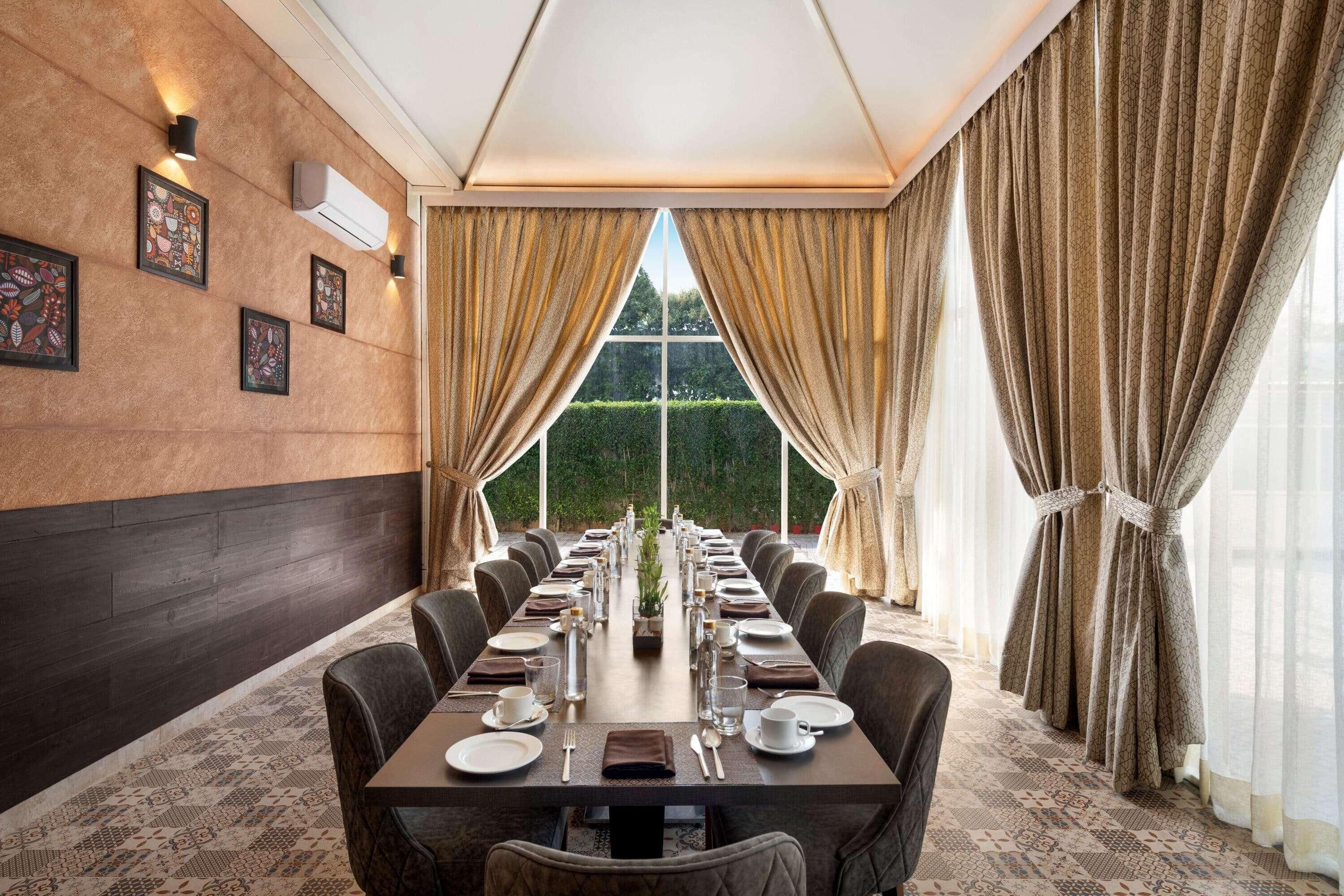 A long dining table set for a meal, with chairs on both sides, in a room with a large window and curtains.