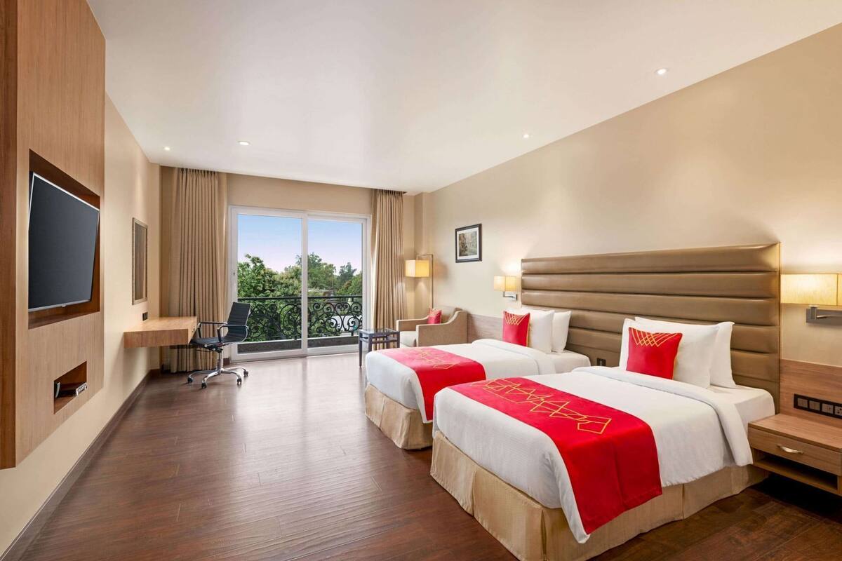 A hotel room with two beds, a desk, a chair, a TV, and a balcony with a view.
