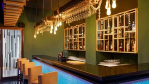 A bar area with a counter, bar stools, hanging light fixtures, and shelves with bottles.