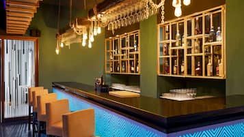 A bar area with a counter, bar stools, hanging light fixtures, and shelves with bottles.