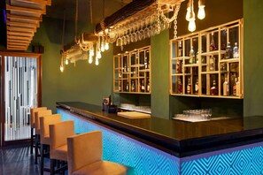 A bar area with a counter, bar stools, hanging light fixtures, and shelves with bottles.