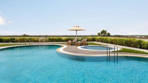 A swimming pool with lounge chairs and an umbrella, surrounded by greenery and a clear sky. - Ramada By Wyndham Aligarh Gt Road (Aligarh)