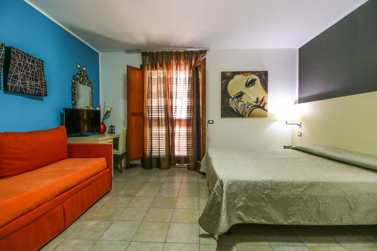 A room with a bed, a sofa, a desk, and a window with curtains.