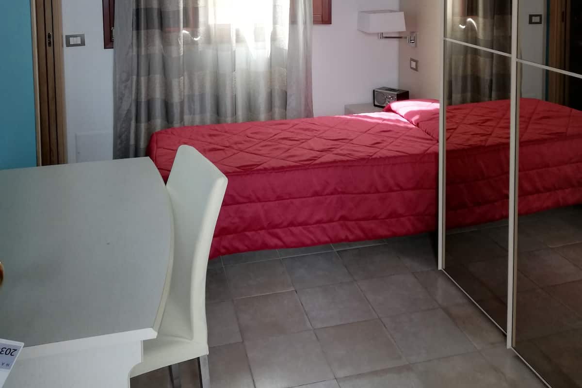 A hotel room with a bed, a TV, an air conditioning unit, a desk, and a chair.