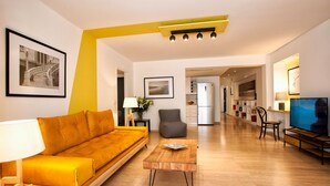 Un soggiorno moderno con un divano, un tavolino, una TV e un'area cucina sullo sfondo.