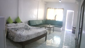 Ein Schlafzimmer mit einem Bett, einem grünen Sofa, einem kleinen Tisch und einem Fenster mit Vorhängen.