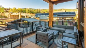 A covered outdoor seating area with modern furniture, a view of the Elk Campground, and a stone wall in the background. - Lumin 3 - Blu Bathworks tubs and Waterworks fixtures. (Snowmass)