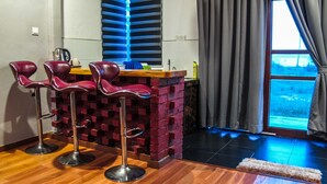 A bar area with three red bar stools, a wooden counter, and a brick accent wall. - Multaqa Suite & Residence (Marang)