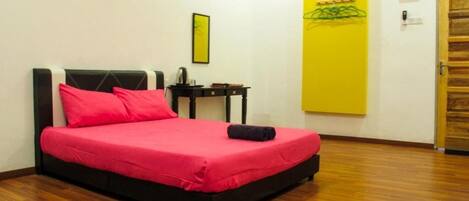 A single bed with a black frame and a red bedspread, a small bedside table with a lamp, a yellow wall decoration, and a wooden door.