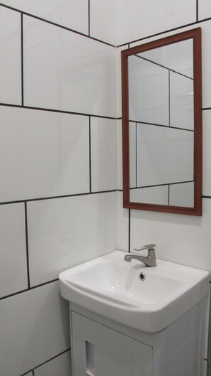 A bathroom with white tiled walls, a white sink, and a wooden-framed mirror.