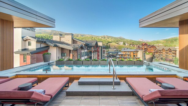 A rooftop pool with lounge chairs, a view of a mountain, and buildings in the background. - One Snowmass West 303 (SNOWMASS VILLAGE)