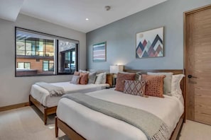 A modern bedroom with two beds, a large window, and artwork on the walls. - One Snowmass West 303 (SNOWMASS VILLAGE)