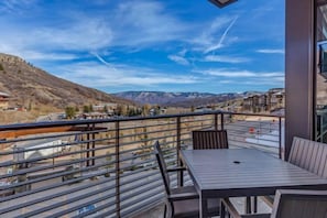 A balcony with a table and chairs, overlooking a mountainous landscape with buildings in the distance. - One Snowmass West 303 (SNOWMASS VILLAGE)