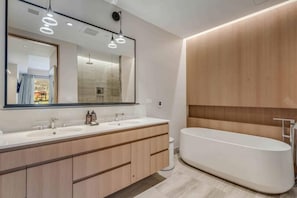 A modern bathroom with a large mirror, two sinks, wooden cabinets, and a freestanding bathtub. - One Snowmass West 303 (SNOWMASS VILLAGE)