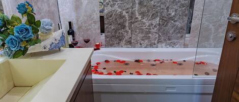 A bathroom with a marble wall, a bathtub with rose petals, and a vase of blue roses.