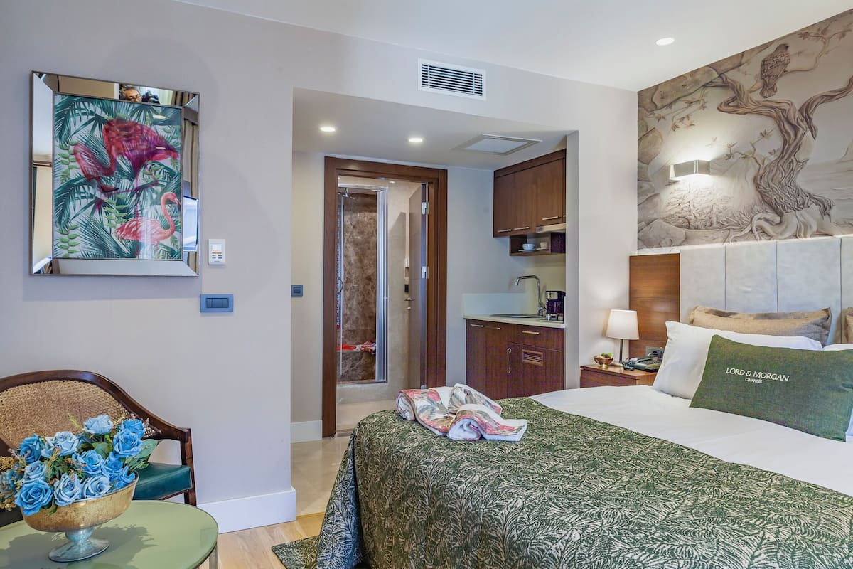 A hotel room with a bed, a desk, a chair, a painting, and a view of the bathroom.