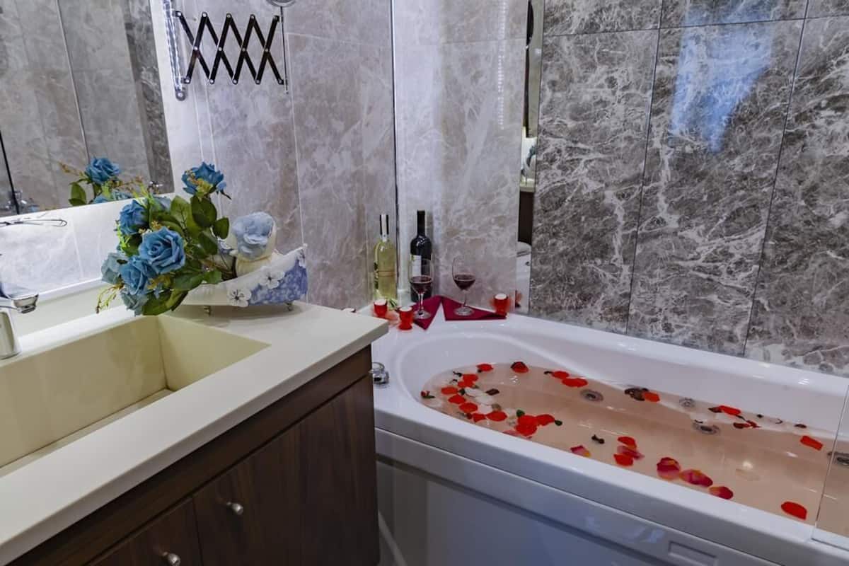 A bathroom with a marble wall, a sink, a bathtub filled with rose petals, and a vase with blue flowers.