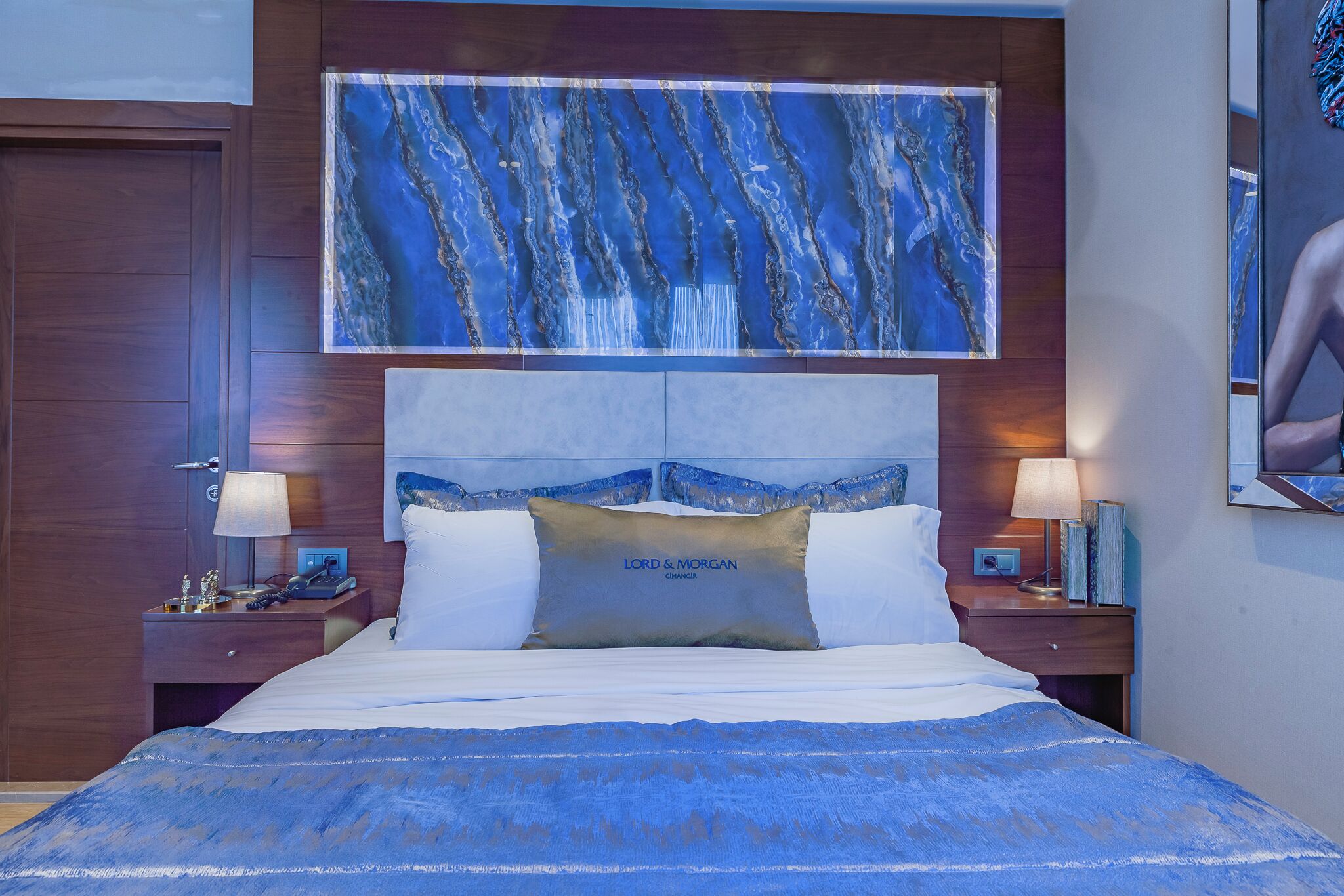 A hotel room with a large bed, two nightstands, a headboard with a decorative panel, and a wall-mounted artwork.