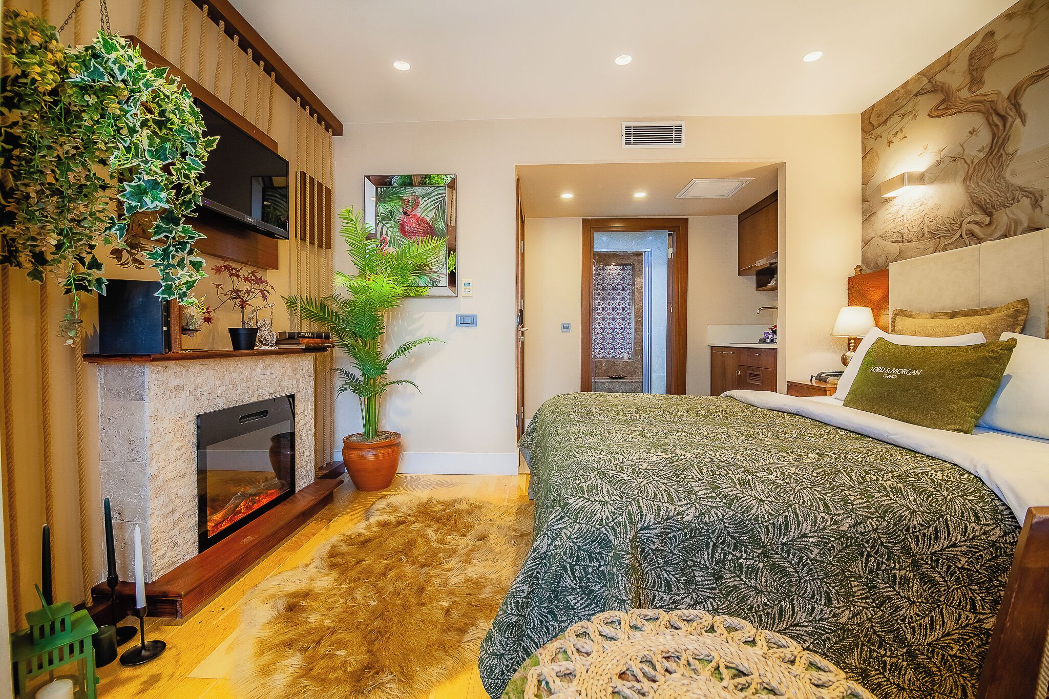 A bedroom with a fireplace, a bed with a patterned bedspread, a green pillow, and a wall-mounted TV.