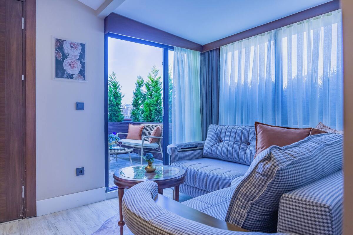 A modern living room with a sofa, armchairs, and a coffee table. There is a sliding glass door leading to an outdoor area with a patio table and chairs.