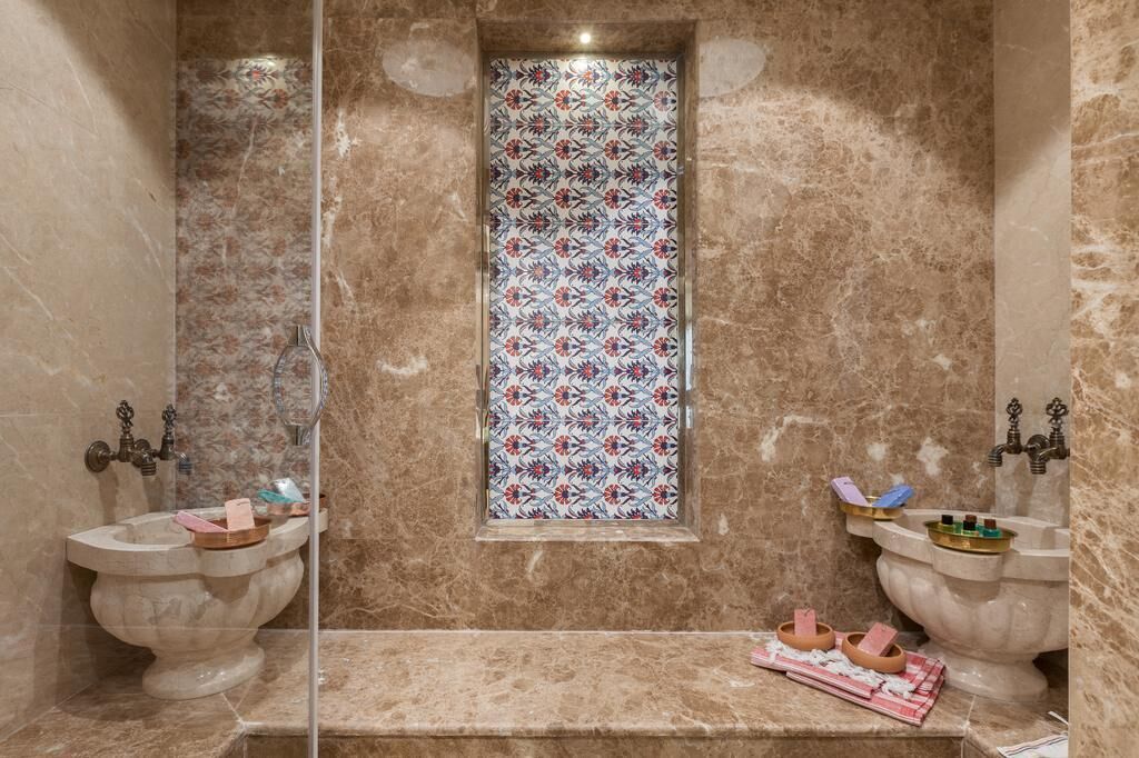 A bathroom with marble walls, a decorative window, and two antique-style sinks with soap and toothbrushes.