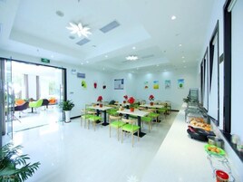 A modern dining area with multiple tables and chairs, a buffet counter with food items, and potted plants on the walls.