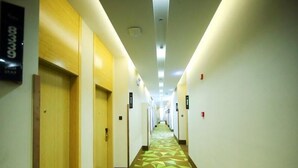 A hotel hallway with doors on both sides, a patterned carpet, and emergency exit signs. - Vaticawuxi Huishan District Western Shengan Road Baile Square Hotel (Wuxi)
