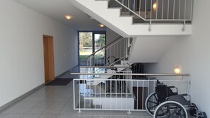 A modern interior with a wheelchair in the foreground, a staircase, and a door leading to an outdoor area.
