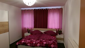 A bedroom with a bed, two bedside tables, a wooden headboard, and pink curtains.
