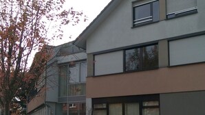 A modern building with a flat roof, large windows, and a paved entrance area with fallen leaves. - Cozy luxury 4 bedroom. In the heart of Heidelberg (Kirchheim)