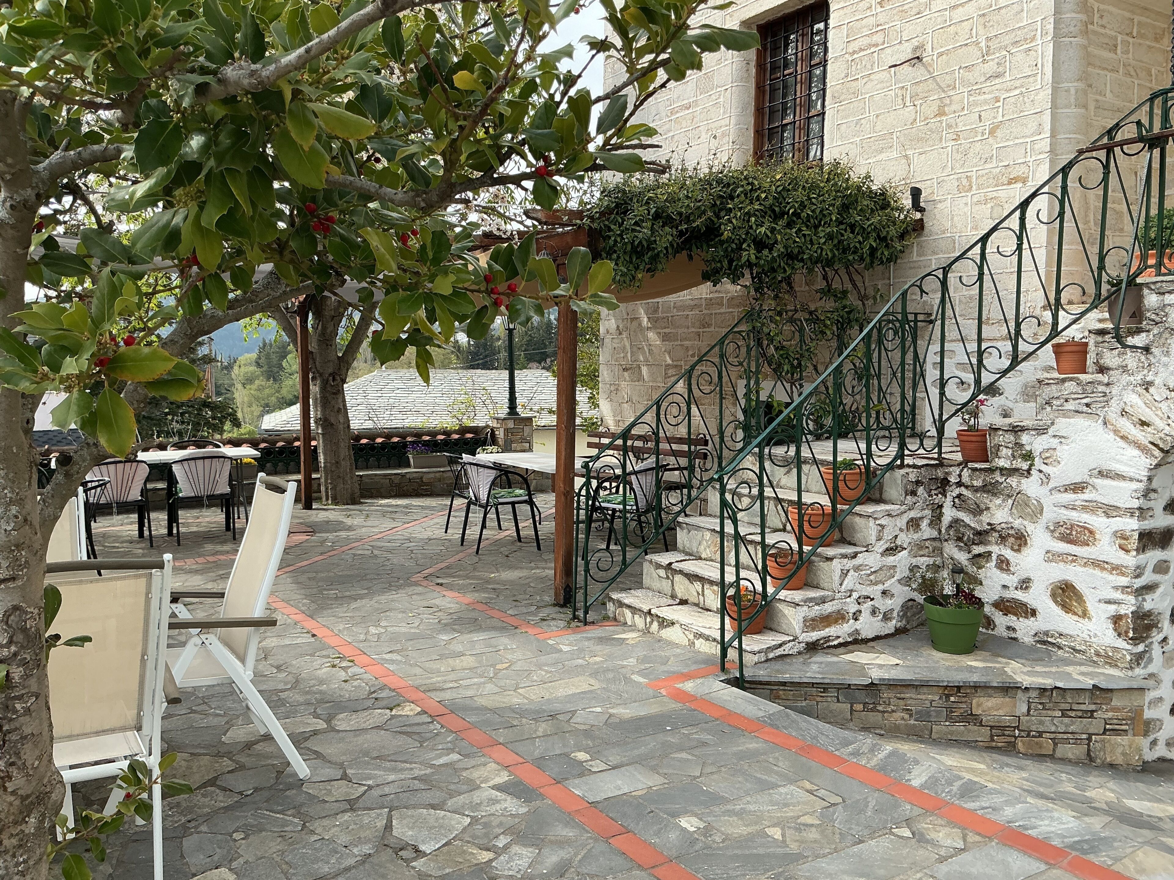 A stone staircase leading to a building with a brick facade, outdoor seating area with tables and chairs, and potted plants.