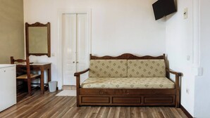 Una habitación con sofá de madera, una mesita, una silla, un espejo y un televisor montado en la pared.