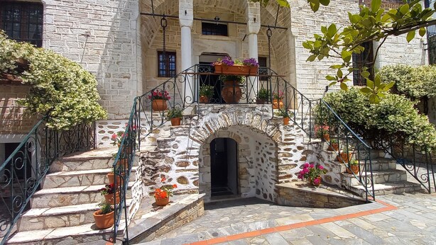 Una escalera de piedra conduce a la entrada de un edificio, rodeada de plantas en macetas y un pequeño arco.