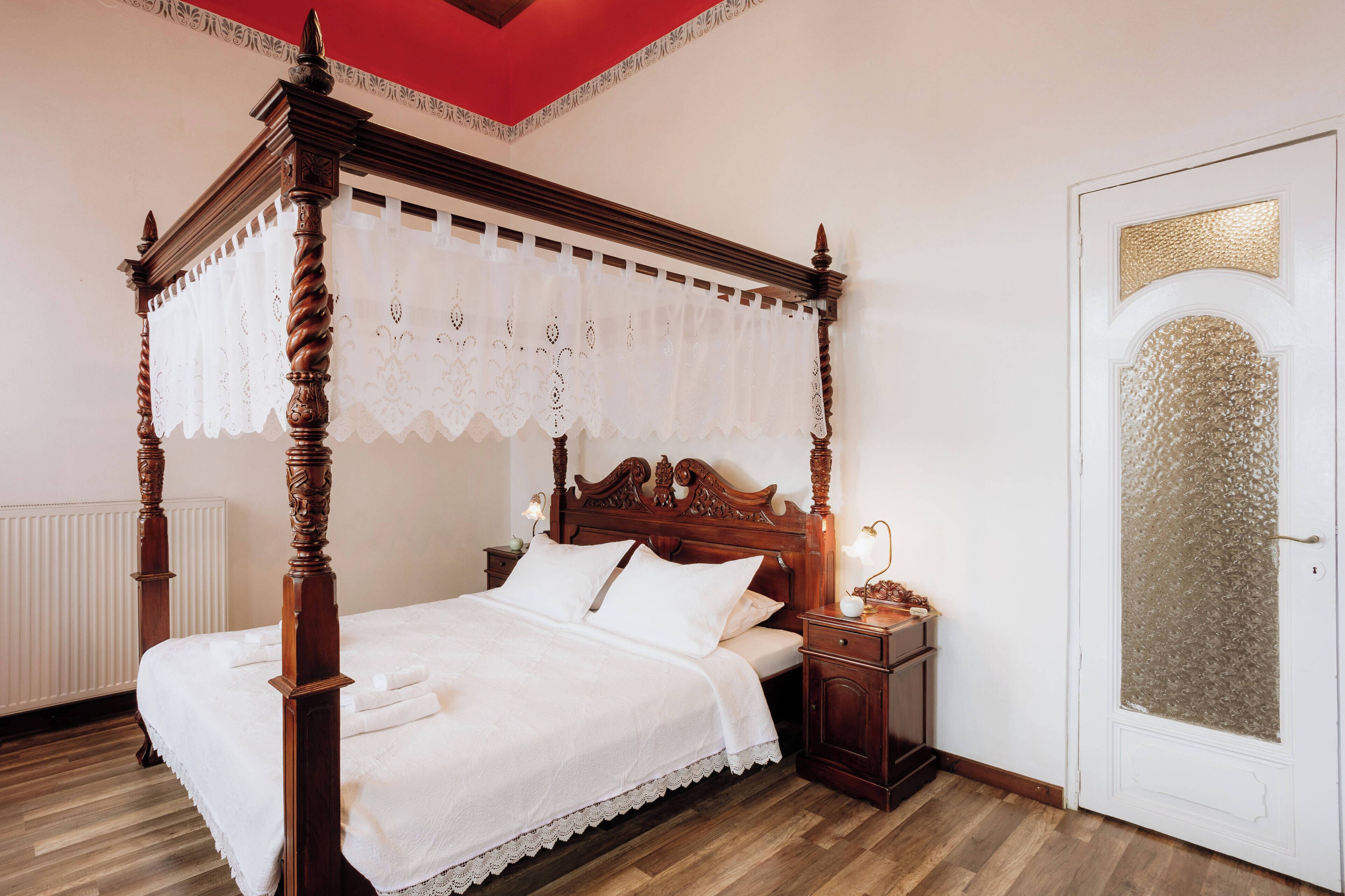 A four-poster bed with a white canopy, a wooden nightstand with a lamp, and a white door with a frosted glass panel.