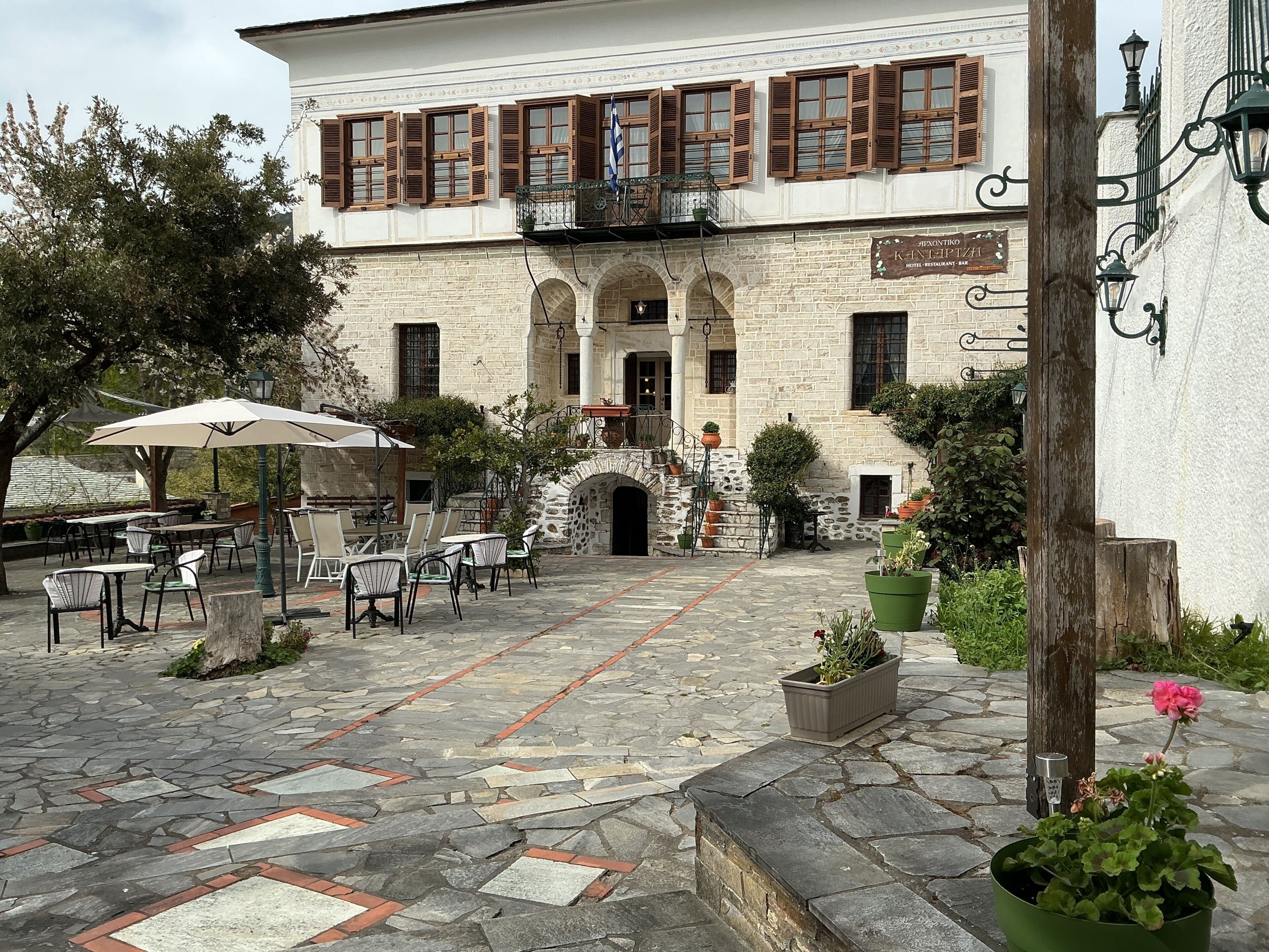 A courtyard with outdoor seating, stone flooring, and a building with a sign indicating a hotel, restaurant, and bar.