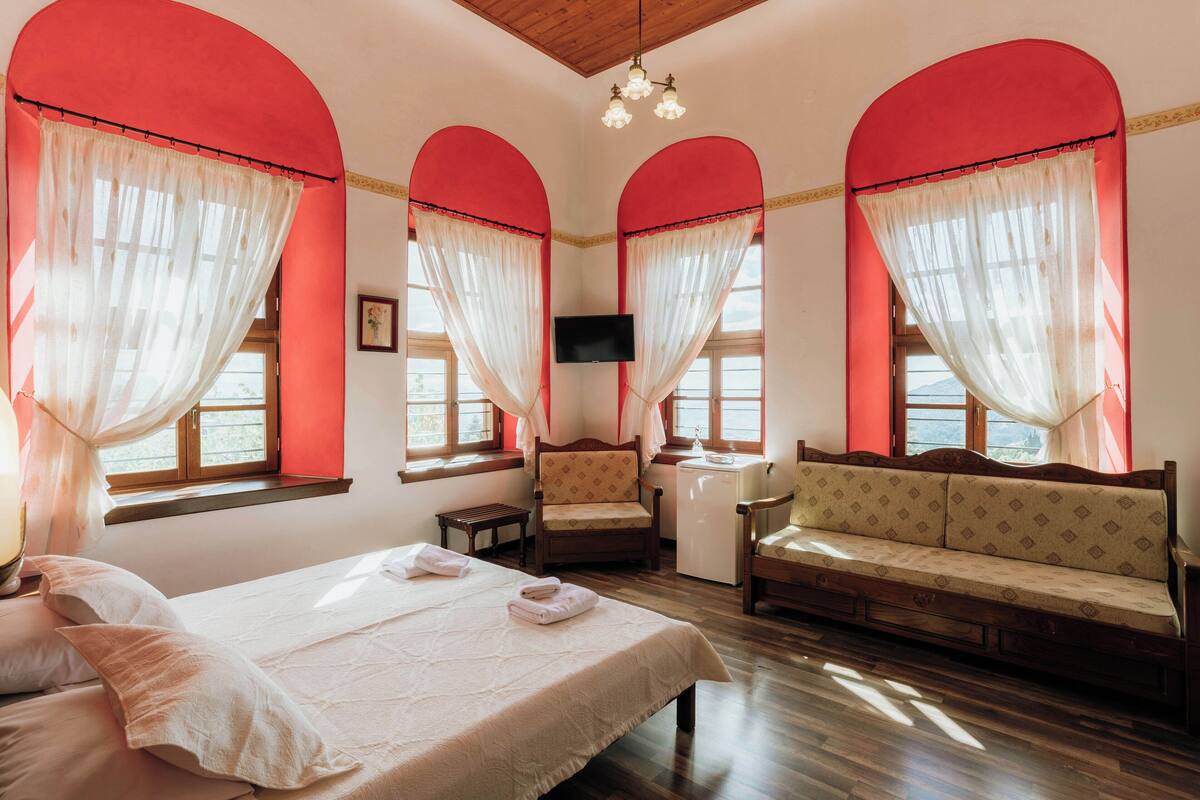 Habitación de hotel con cama, sofá, sillón, televisor y escritorio.