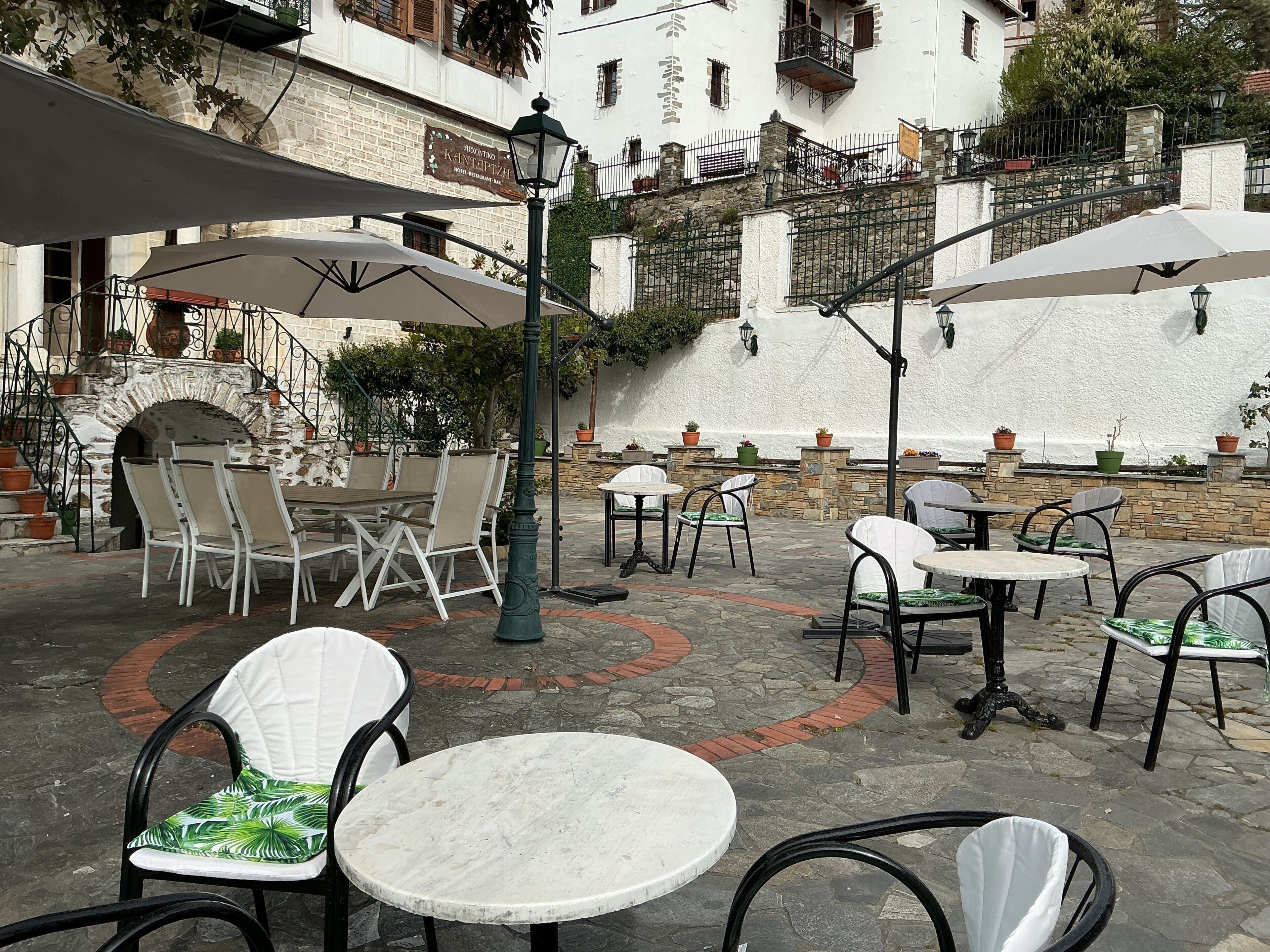 An outdoor patio area with tables and chairs, a stone wall, and a sign indicating a restaurant.