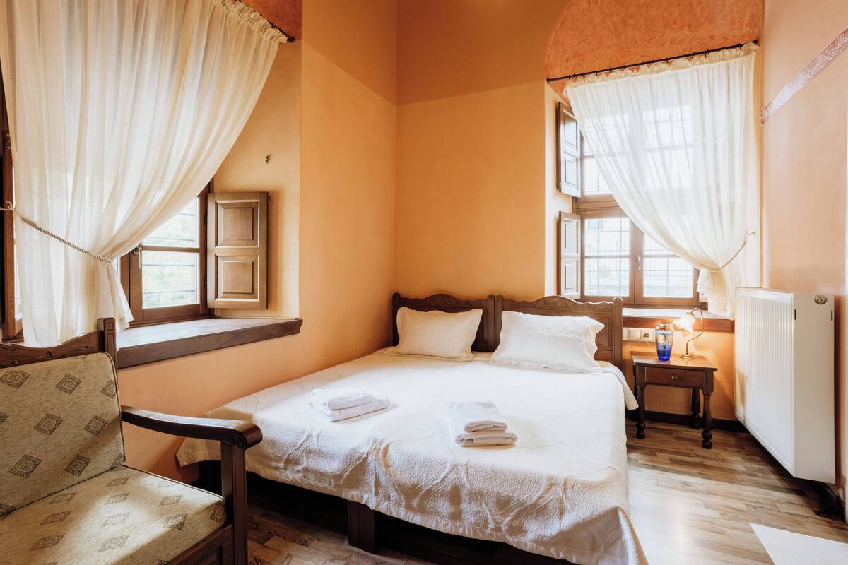 Un dormitorio acogedor con una cama grande, una silla de madera y una mesita de noche con una lámpara.