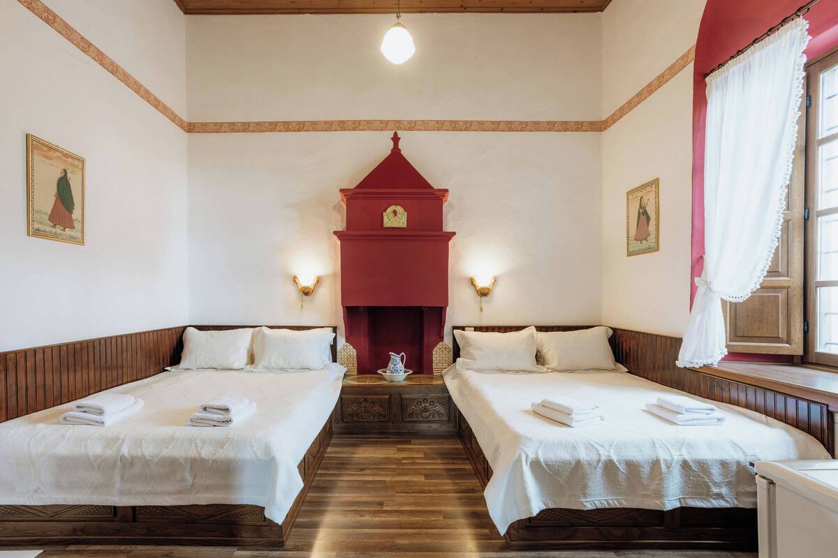Habitación de hotel con dos camas, cabeceros de madera, un detalle en la pared de color rojo y luces fijadas a la pared.