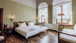 Un dormitorio con una cama grande, dos mesitas de noche, una silla y un ventanal con cortinas.