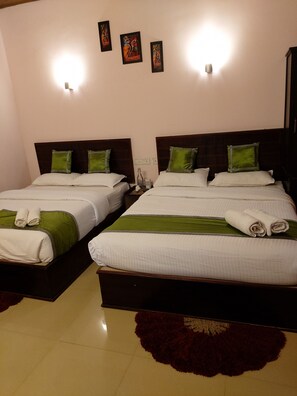 Two double beds with green and white bedding, a small table with a bottle and a cup, and a decorative rug on the floor. - Happy valley Home stay (Chithirapuram)