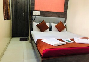 A neatly made bed with white linens and brown pillows, a red throw blanket, and a small bedside table with a book and a tissue box. - Hotel Sun Star Residency (Mumbai)