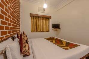 A hotel room with a brick-patterned wall, a bed with white bedding and a patterned throw, a television on a stand, and a window with curtains. - Hotel Sun Star Residency (Mumbai)