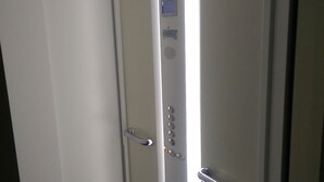Ein schmales Aufzug mit digitaler Anzeige, Bedienfeld und einem Metallhandlauf.