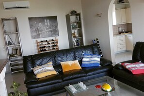 A living room with a black leather sofa, a chessboard, and a coffee table. There is a bookshelf with various items and a framed picture on the wall. - Villa with panoramic view (CORFU)