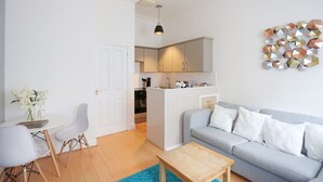 Een moderne woonkamer met een grijze bank, een houten salontafel en een eethoek met witte stoelen en een kleine tafel.
